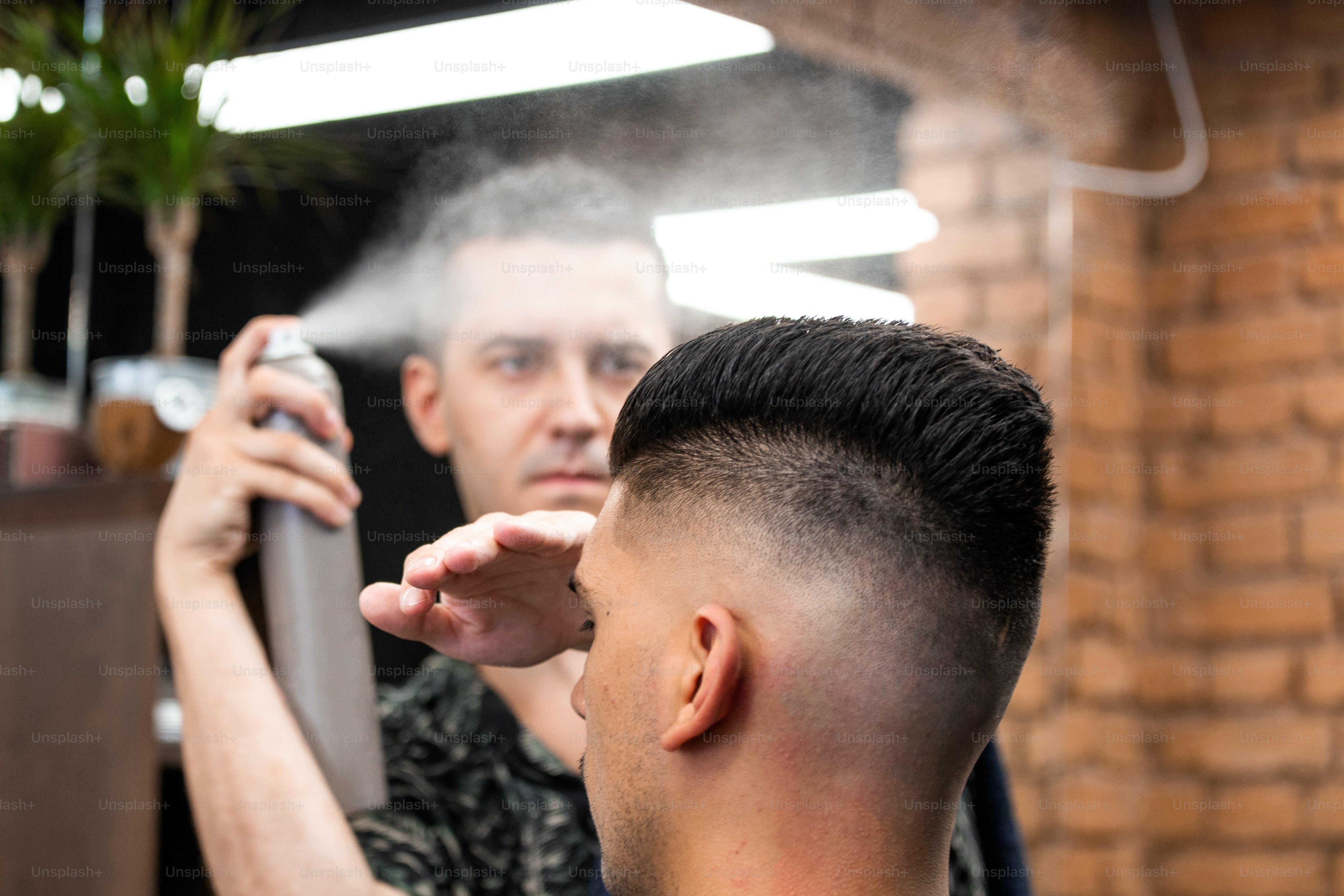 Professional Hairdresser using hair spray on client hair at barber shop, Cool barber splashes from the spray bottle at the hair of his client.